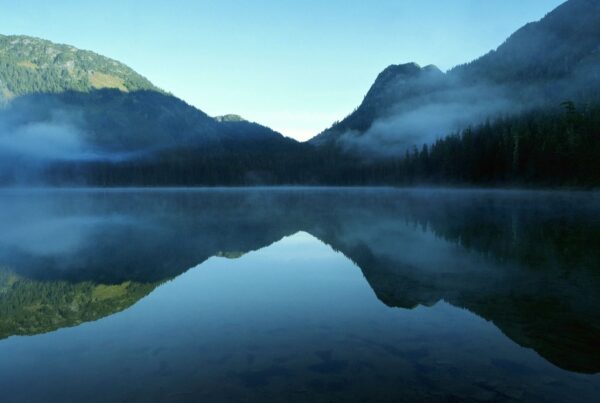 Lake surrounded by rolling mountains with some light fog.